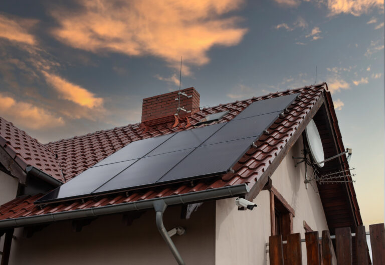 A low angle shot of a house with solar panels on the roof under a sunset sky
